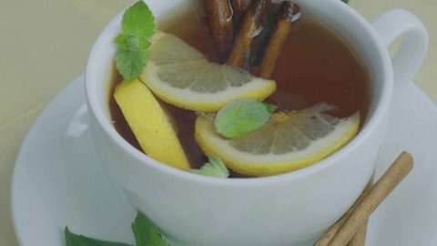Black and green tea with lemon, cinnamon sticks and mint leaves rotating. Hot drink. Healthy melissa tea natural organic aromatic drink in cup. Summer, Autumn winter warming drink.