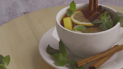 Black and green tea with lemon, cinnamon sticks and mint leaves rotating. Hot drink. Healthy melissa tea natural organic aromatic drink in cup. Summer, Autumn winter warming drink.