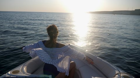 brunette woman in a striped shirt floats hand up on the bow of a fast boat at sunset