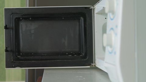 Close-up shot of a person cleaning a microwave with vinegar. Housewife hand in rubber gloves cleans microwave oven. Old microwave cleaning