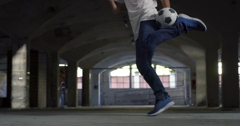 Cinematic shot of young carefree arab freestyle soccer player is  juggling sport ball with his knee and feet while training tricks of self-expression with football in public underground parking.