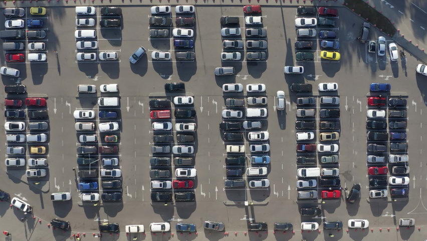 A lot of Cars moving around busy Parking lot near Big Shopping Center searching for a free parking place. 