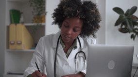 Doctor telehealth remote service. Spbas Attentive young African-American woman general practitioner consults patient writing complaints during videochat in hospital