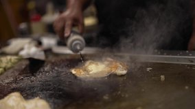 This video shows a close up view of a chef adding sauces to a grilling fish fillet and flipping it over to cook.