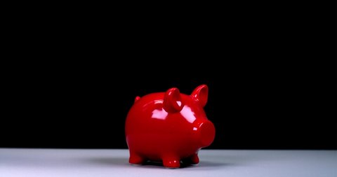 A man's hand smashes a red piggy bank in the shape of a pig with a hammer, fragments and coins fly in different directions, slow motion against a bright background