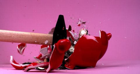 A hammer breaks a red piggy bank in the shape of a pig, shards and coins fly in different directions, slow motion against a bright background