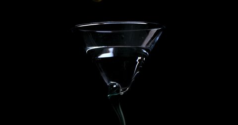 Olive falling into a glass with martini on a black background in slow motion