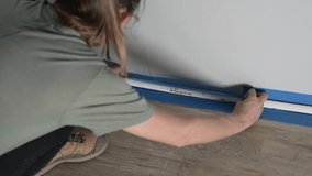 This video shows a young caucasian woman masking off a residential home wall and trim for painting.