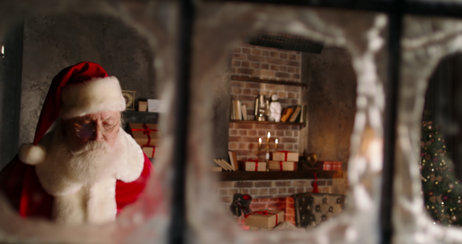 Santa Claus looking out window close-up, staring outside, taking bag full of presents for children. Christmas and New Year concept. Happy holidays and winter traditions. 