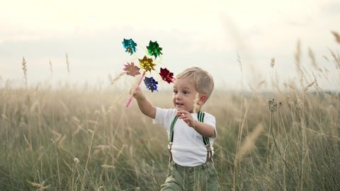 Happy kid with toy in park. Toy windmill in hand of child. Happy kid run over spikelets. Little hand of child is holding toy windmill. Kid plays in park. Happy childhood concept. Happy kid run in park