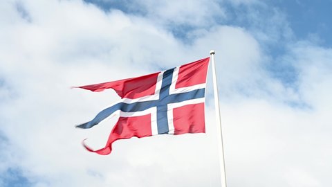 Waving national flag of Norway under a partly-cloudy sky.
