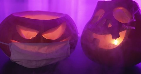 Two spooky pumpkins glowing inside jack lantern face with smoke at neon pink blogger background. Orange carved pumpkin with medical mask in fog. Jack-o-lantern glows on Halloween. Covid pandemic.