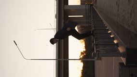 Successful young businessman in jacket and with business briefcase in his hands is doing back somersault. Businessman or office worker makes a spectacular trick against backdrop sunset. Vertical video