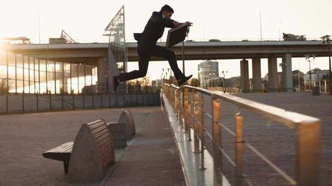Successful young businessman runs overcoming obstacles in front of him. Entrepreneur or office worker rushing to work jumping over obstacles on the way. Stuntman in classic clothes. Slow motion