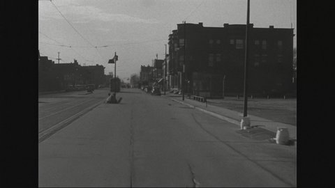 1940s: View from car driving down South Chicago Street lined with small businesses. Trolley car. Motorcycle with side car drives in front of car.