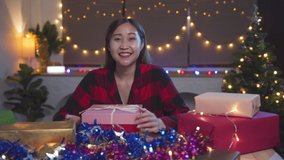 Smiling Asian young woman holding Christmas Gift box and using laptop as webcam for video call