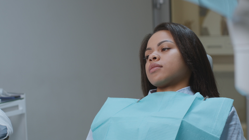Fear of dentist. Young afraid african american woman sitting at dental clinic and rejecting doctor with tools, suffering from dentophobia attack, slow motion Royalty-Free Stock Footage #1080181991