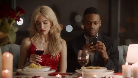 Infidelity In Marriage. Cheating Husband Texting On Phone During Romantic Dinner With Wife Sitting In Fancy Restaurant At Night. Girlfriend Suspecting Affair While Boyfriend Using Smartphone