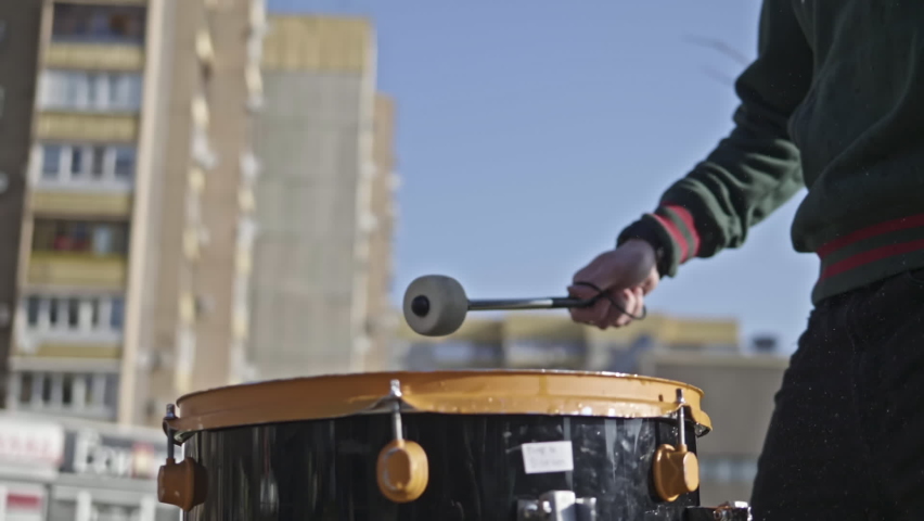 A man beats a drum on the street. Slow motion shot of drum hit and splashing water. Drummer plays, hitting drums with water on it.
