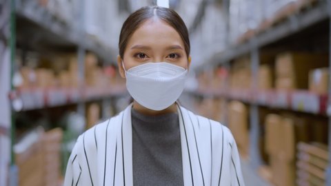 business is now running, asian female business owner look at camera taking facemask off smile with cheerful confident in warehouse storage full of product boxes shelf distribution inventory factory