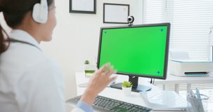 back view of female doctor wearing headset having video call by computer with green screen