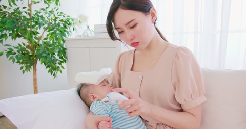 authentic shot of asian baby has fever and his mother checks temperature by thermometer on sofa