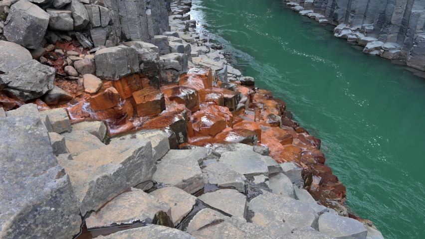 Reveal of orange-grey basalt canyon with a green massive river flowing between steep rocky columns