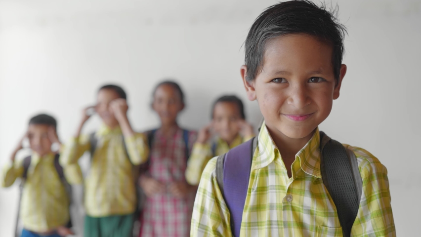 close shot of a young little adorable primary school boy wearing a uniform with backpack smiling joyfully staring at the camera standing in classroom learning and education concept Royalty-Free Stock Footage #1080199592