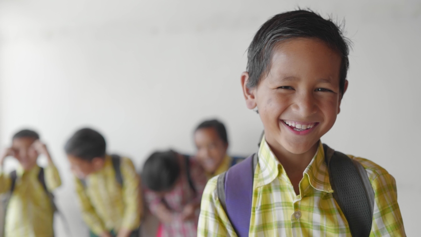 Close shot of a young little adorable primary school boy wearing a uniform with backpack smiling joyfully staring at the camera standing in classroom learning and education concept | Shutterstock HD Video #1080199592