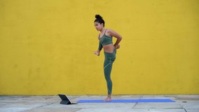 Positive newbie in yoga training woman using digital tablet for practising laughing at troubles during class,cheerful unprofessional female in tracksuit having fun trying to replicate poses