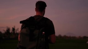 Caucasian male traveler with backpack using smartphone camera for making picture and shooting content for sharing in social networks during evening dusk on tropical destination