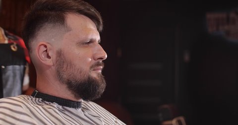 Close-up of a handsome Caucasian guy sitting in a hairdressing salon. An unrecognizable barber brushes off bobbed hair and makes styling. 4K 50 fps slow motion
