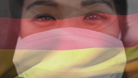 Animation of flag of germany waving over woman wearing face mask during covid 19 pandemic. global covid 19 pandemic concept digitally generated video.