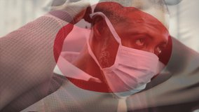 Animation of flag of japan waving over man wearing face mask during covid 19 pandemic. global covid 19 pandemic concept digitally generated video.