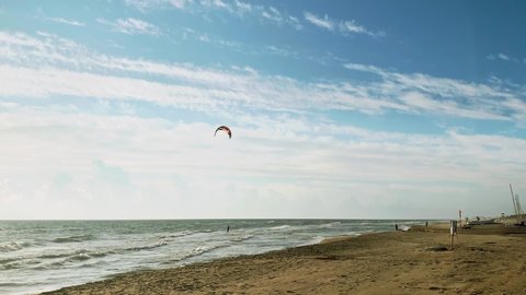 Kitesurfer on the crest of a wave. Blue sky with white clouds. Seascape with kitesurfers in the waves. Colorful kitesurfing sail fly in the cloudy sky. 