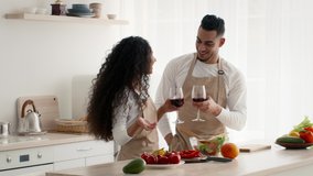 Happy Arabic Couple Drinking Wine Flirting And Hugging Preparing Dinner Standing In Modern Kitchen At Home. Middle-Eastern Millennial Spouses Enjoying Cooking Together. Slow Motion