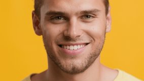 Closeup Portrait Of Handsome Young Blonde Guy Looking At Camera And Smiling, Cheerful Attractive Millennial Man Posing Over Yellow Studio Background, Expressing Positive Emotions, Slow Motion Footage