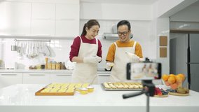 4K Asian couple bakery shop owner using smartphone with internet vlogging sweet dessert baking on social media together in the kitchen. Small business entrepreneur and online cooking class concept