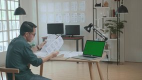 Creative Designer Works On A Storyboard, Looks At His Sketches With Mock Up Green Screen Laptop Computer, Choosing The Best Drawings For His Project, Comics Compilation, Application Ui Or Game Plot
