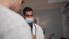 Male nurse holding tablet wearing surgical mask explaining to patient