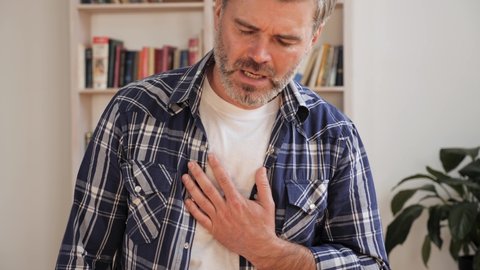 Trouble breathing, chest pain, adult man at home office having difficulty breathing pain of heart, touches his chest with hand. Heart attack, thoracic osteochondrosis, panic attack concept.