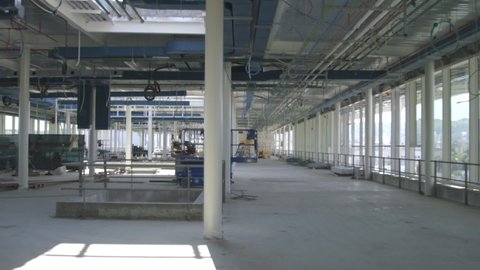 Camera panning in interior room of a big industrial building under construction. Supplies, tools, materials, scissor lift. Panoramic view from windows. Nobody in.
