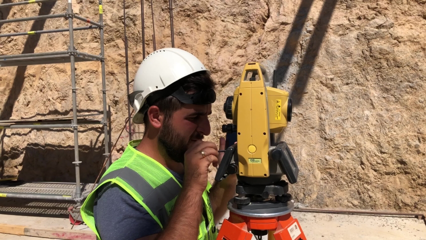 Geodetic or topographic works at construction site. Land surveyor doing a measurements on total station. Topographer looks to theodolite telescope Royalty-Free Stock Footage #1080233663