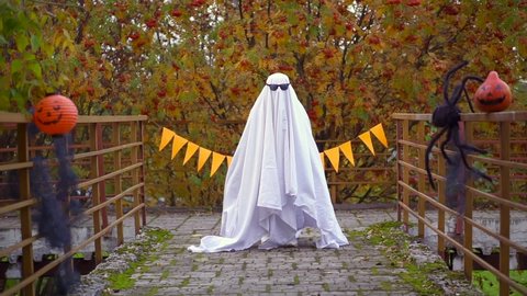casting dance in glasses. ghost halloween. man in white sheet runs in street. Fancy dress flies. Funny witch jump. concept of holiday in carnival costume in fall. Orange pumpkin and spider. terrible