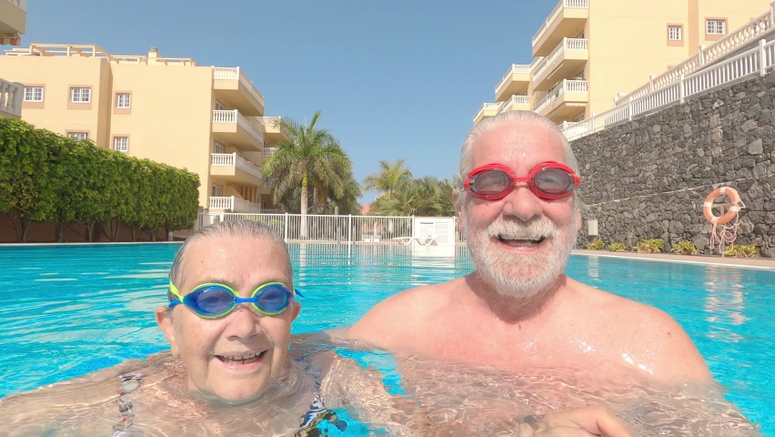 Couple of two happy seniors having fun and enjoying together in the swimming pool smiling and playing. Happy people enjoying summer outdoor underwater waving Royalty-Free Stock Footage #1080243443
