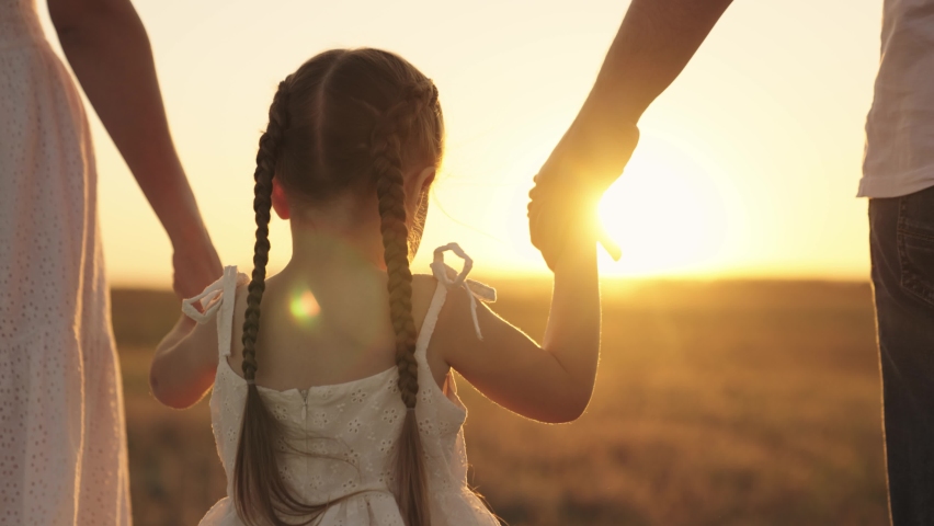 cheerful girl holding her parents' hands at sunset in sky, happy family, childhood dream, child with mom and dad in sun, little kid walks with father mother, family day, travel with baby hand in hand Royalty-Free Stock Footage #1080244313