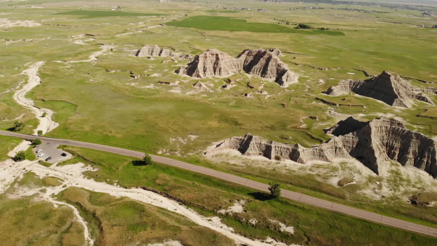Drone Aerial View of Cars on Road in Badlands National Park, South Dakota, USA. Sandstone Rock Formations and Green Prairie on Sunny Day