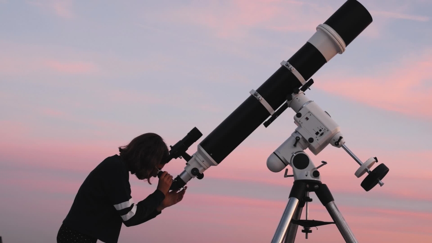 Silhouette of a small girl child, telescope  under the twilight skies.