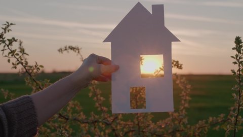 holding a paper house at sunset, a mortgage loan to a young family, a ray of sunlight shining through the window, purchasing a new home, moving into home ownership, renting real estate for living