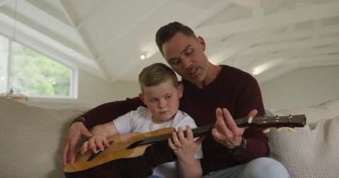 Caucasian father with son playing guitar together and sitting in living room. family spending time at home.